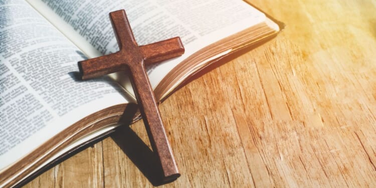 A close up of a small cross leaning against an open Bible.