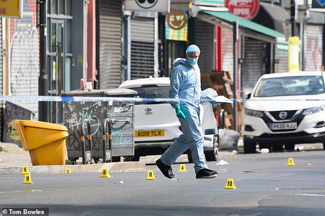 Investigators wearing blue overalls, masks and gloves inspect the scene on Coldharbour Lane in Brixton, south London