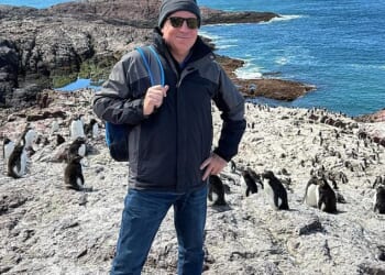 Fraser Allen (pictured with a penguin colony in Chile), 58, has spent the past one and a half years living on a cruise ship