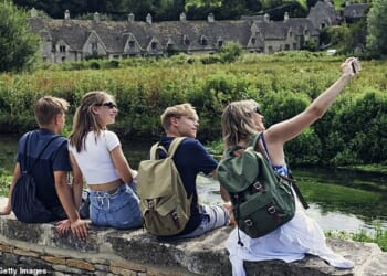 A family take a selfie outside Arlington Row's 17th century weaver cottages in Bibury in the Cotswolds