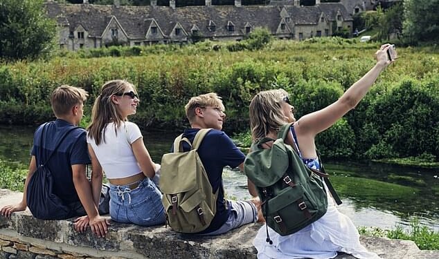 A family take a selfie outside Arlington Row's 17th century weaver cottages in Bibury in the Cotswolds